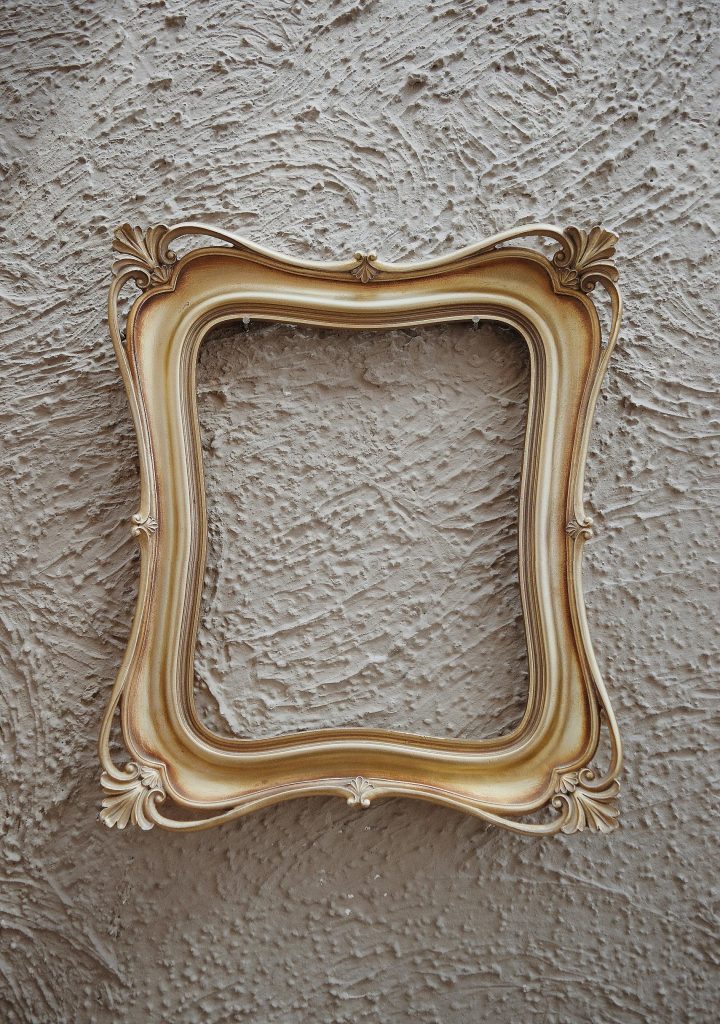 Antique golden frame with ornate details against a textured gray wall, perfect for art and design themes.